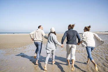 Familie hält sich beim Laufen am Strand an den Händen - UUF21718