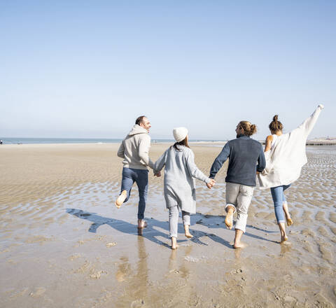 Playful family holding hands while running at beach stock photo