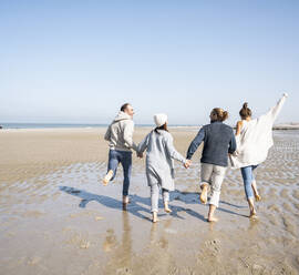 Verspielte Familie hält sich beim Laufen am Strand an den Händen - UUF21719