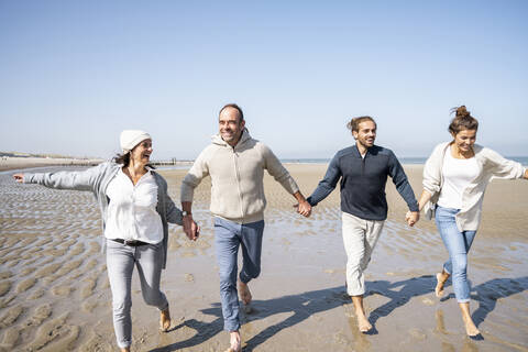 Happy young and mature couple holding hands while running on beach stock photo