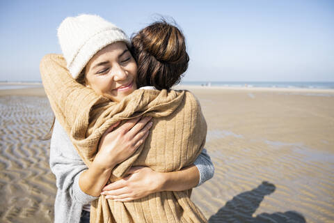 Daughter and mother embracing each other while standing at beach stock photo