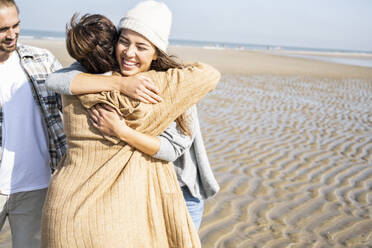 Mother and daughter embracing while standing by man at beach - UUF21729