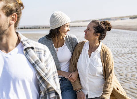 Man walking with women holding hands in background at beach stock photo