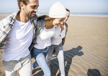 Couple and mother walking with arm around at beach - UUF21734