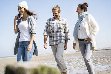 Smiling woman walking with boyfriend and mother at beach - UUF21742