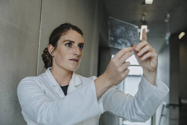 Female scientist examining human brain glass sample while standing at clinic corridor - MFF06322
