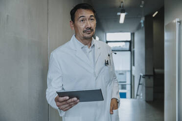 Scientist with hand in pocket using digital tablet while standing at clinic corridor - MFF06355