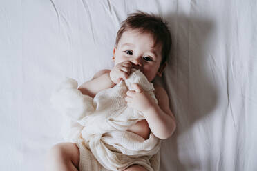 Cute baby boy holding towel while lying on bed in bedroom at home - EBBF00873