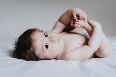 Babyjunge berührt die Beine, während er auf dem Bett liegt - EBBF00875