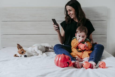 Mutter schreibt eine SMS auf ihrem Smartphone, während ihr Sohn zu Hause mit Spielzeug spielt - EBBF00877