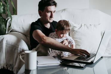 Father using laptop while son sitting on his lap at home - EBBF00881