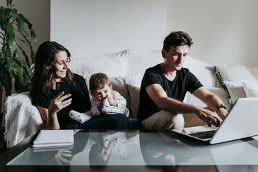 Lächelnde Mutter, die ein Smartphone benutzt, während der Vater am Laptop arbeitet und der Sohn zu Hause sitzt - EBBF00895