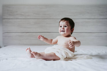 Cute baby boy looking away while sitting on bed at home - EBBF00899