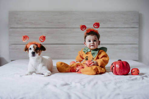 Nettes Baby und Hund tragen Halloween-Kostüm sitzen auf dem Bett zu Hause - EBBF00911