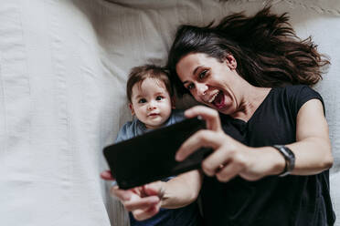 Mutter und Sohn machen ein Selfie mit dem Smartphone, während sie zu Hause im Schlafzimmer liegen - EBBF00917