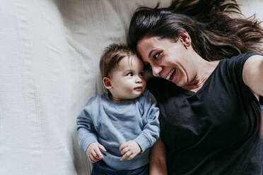 Lächelnde Mutter und Sohn, die ein Selfie machen, während sie zu Hause auf dem Bett liegen - EBBF00918