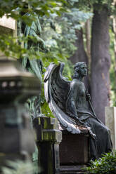 Weathered statue of angel sitting at edge of tomb in cemetery - JATF01248