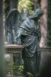 Weathered statue of angel standing beside tomb in cemetery - JATF01251