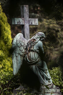 Verwitterte Statue eines Engels neben einem Kreuz auf einem Friedhof - JATF01253