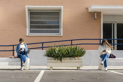 Female teenage friends using smart phone while sitting on concrete bench - ERRF04568