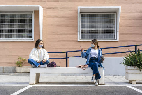 Friend taking picture of teenage girl sitting on concrete bench - ERRF04570