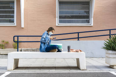 Teenage girl taking picture of notes while sitting on concrete bench - ERRF04574