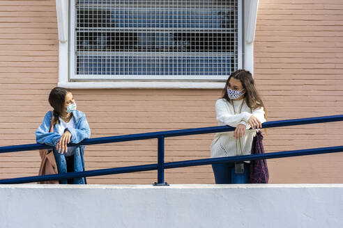 Female teenage friends looking at each other while leaning on railing during covid-19 - ERRF04579