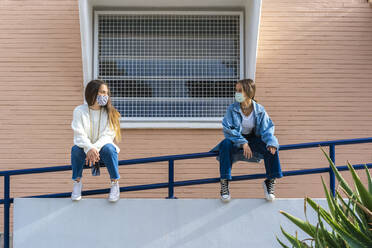 Female friends looking at each other while sitting on railing - ERRF04583