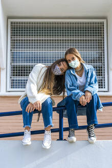 Teenage girl head on female friend's shoulder sitting during sunny day - ERRF04586