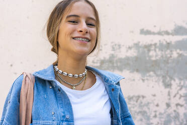 Smiling teenage girl standing against wall - ERRF04588