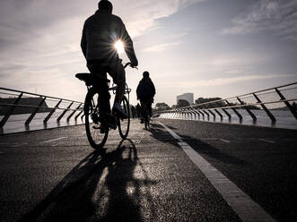 Dänemark, Kopenhagen, Silhouetten von zwei Menschen auf Fahrrädern über die Langebro-Brücke bei Sonnenuntergang - HAMF00722