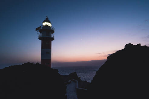 Low Winkel der spektakulären Landschaft der beleuchteten Leuchtturm auf felsigen Hügel in der Nähe von Meer gegen Sonnenuntergang Himmel in Teneriffa gelegen - ADSF16672