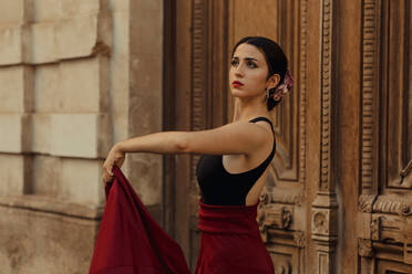 Charmante junge hispanische Brünette in rotem Rock führt traditionellen Flamenco-Tanz in der Nähe von Holztür des alten Gebäudes - ADSF16697