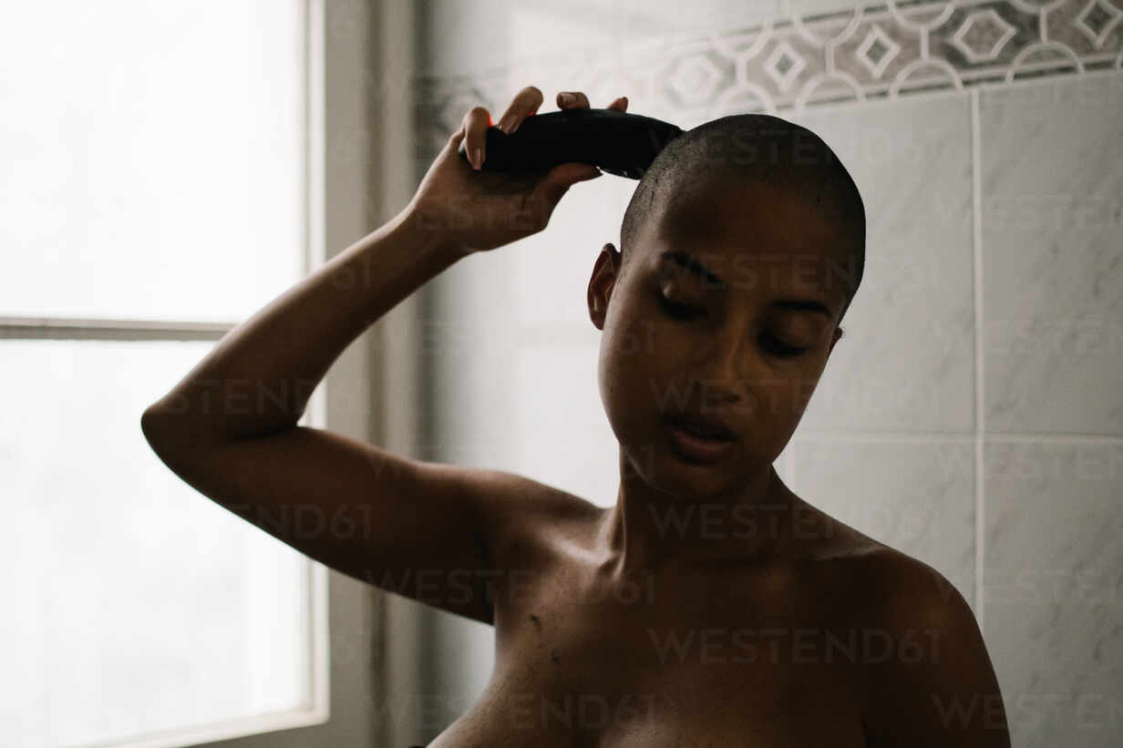 Focused African American female in lingerie standing in bathroom and using  trimmer for cutting hair stock photo
