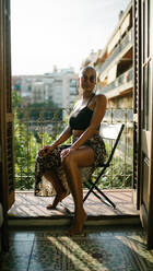 Low angle of black female with bald hairstyle and in trendy outfit sitting on terrace of outdoors cafe and relaxing while looking at camera - ADSF16706