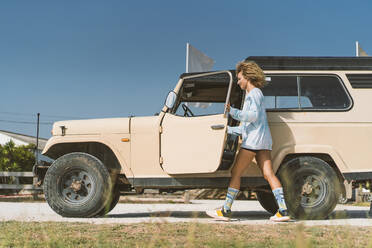 Young Afro woman by old off-road vehicle on sunny day - DAMF00585