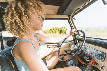 Young blond Afro woman sitting in old off-road vehicle - DAMF00587