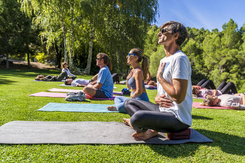 Ältere männliche und weibliche Touristen üben Yoga auf einer Matte in einem Gesundheitszentrum an einem sonnigen Tag - DLTSF01360