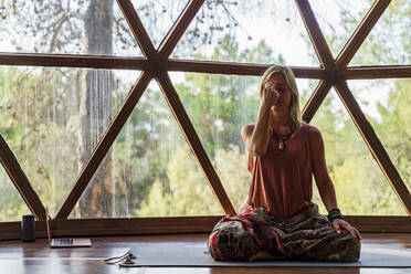 Reife Yogalehrerin meditiert gegen das Fenster im Wellnessbereich - DLTSF01393