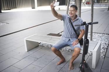 Reifer Mann, der ein Selfie macht, während er auf einer Bank sitzt - HMEF01104