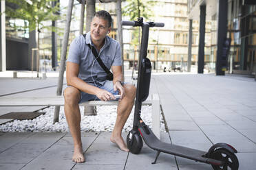 Mature man looking away using smart phone while sitting on bench - HMEF01105