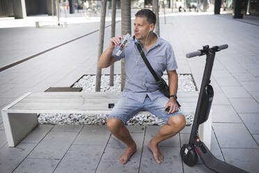 Mature man looking away while drinking water sitting on bench - HMEF01106