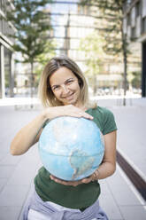 Mittlere Frau hält Globus, während sie auf dem Fußweg in der Stadt steht - HMEF01112