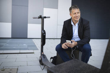Älterer Geschäftsmann, der ein Smartphone benutzt und Musik hört, während er auf einer Bank sitzt - HMEF01120