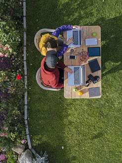 Couple sitting in garden, using laptop at tables - KNTF05798