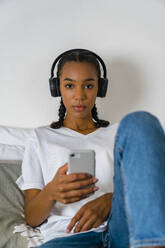 Junges Mädchen im Teenageralter hört Musik über Kopfhörer am Smartphone zu Hause - MGIF01019