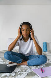 Teenage girl with cross legged listening to music while sitting at home - MGIF01025