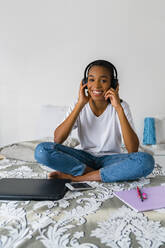 Smiling teenage girl with cross legged listening to music while sitting at home - MGIF01026