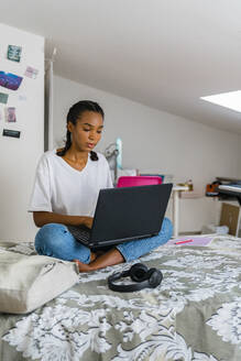 Teenager-Mädchen benutzt einen Laptop, während sie zu Hause sitzt - MGIF01028