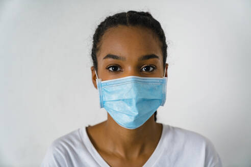 Teenager-Mädchen mit Gesichtsschutzmaske, das während des Covid-19 an der Wand steht - MGIF01034